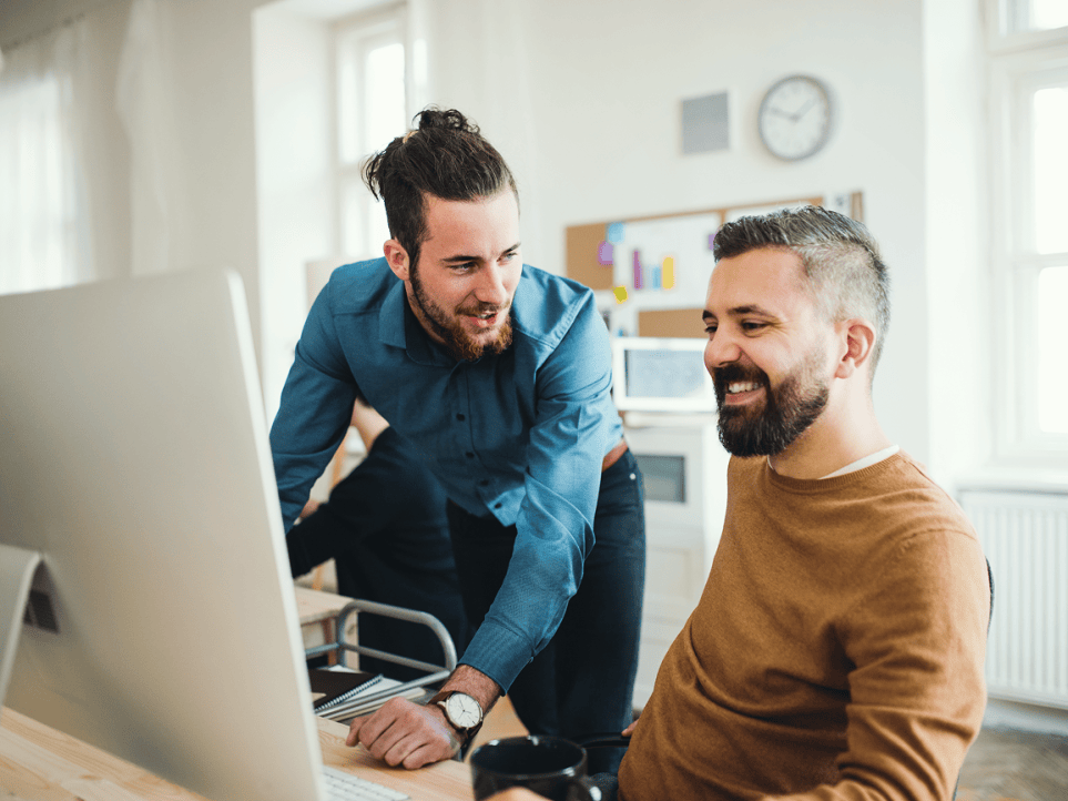 Two men are talking at a workstation.