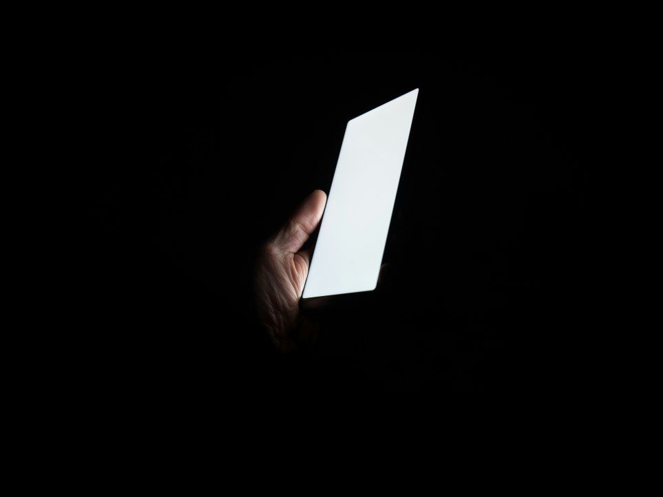 Hand hält ein Smartphone mit leuchtendem Display. Hintergrund des Bildes ist dunkel.