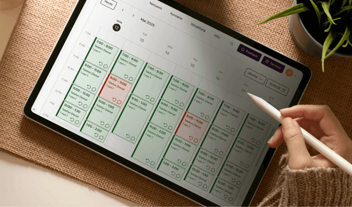 Sicht von oben auf einen Schreibtisch, auf dem die Hand einer Person einen Stift hält und auf einem Tablet arbeitet. 