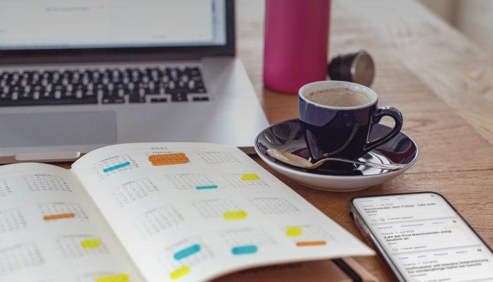 Notizbuch mit Agenda/Kalender, Kaffee und Telefon auf einem Tisch, der die Rolle von dpa-Agenda bei der Planung von Medienberichten und PR-Strategien repräsentiert.