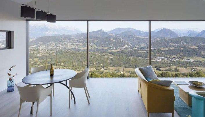 Panoramablick aus einem Zimmer heraus durch eine Glaswand von Finstral mit Bergen im Hintergrund.