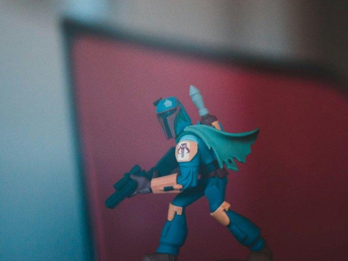 Actionfigur eines Charakters im Mandalorianer-Stil vor einem unscharfen roten Hintergrund.