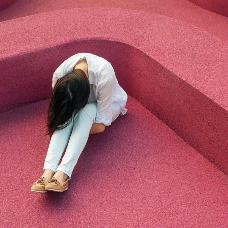 Woman sitting alone with head down on abstract pink structure – business analysis and IT consulting visualized through image of emotional crisis and support.