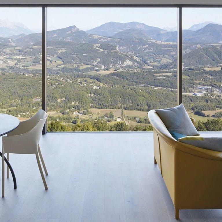 Panoramablick aus einem Zimmer heraus durch eine Glaswand von Finstral mit Bergen im Hintergrund.