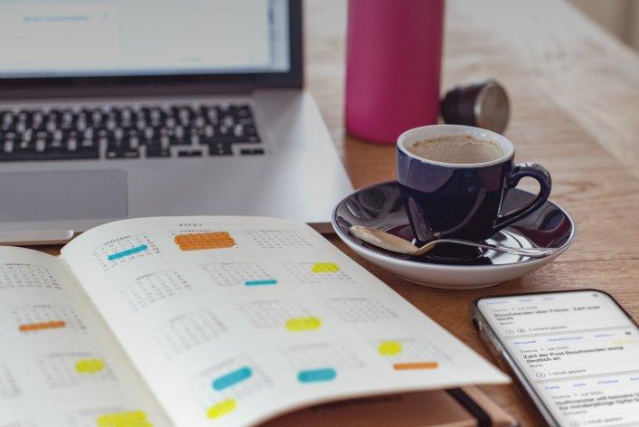 Notizbuch mit Agenda/Kalender, Kaffee und Telefon auf einem Tisch, der die Rolle von dpa-Agenda bei der Planung von Medienberichten und PR-Strategien repräsentiert.