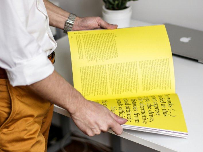 Eine stehende Person, die ein Buch mit gelben Seiten liest