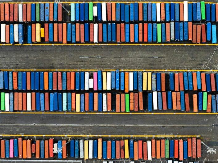 Luftaufnahme von ordentlich angeordneten, farbcodierten Schiffscontainern in parallelen Reihen, die strukturiertes digitales Asset Management und systematische Organisation symbolisieren.